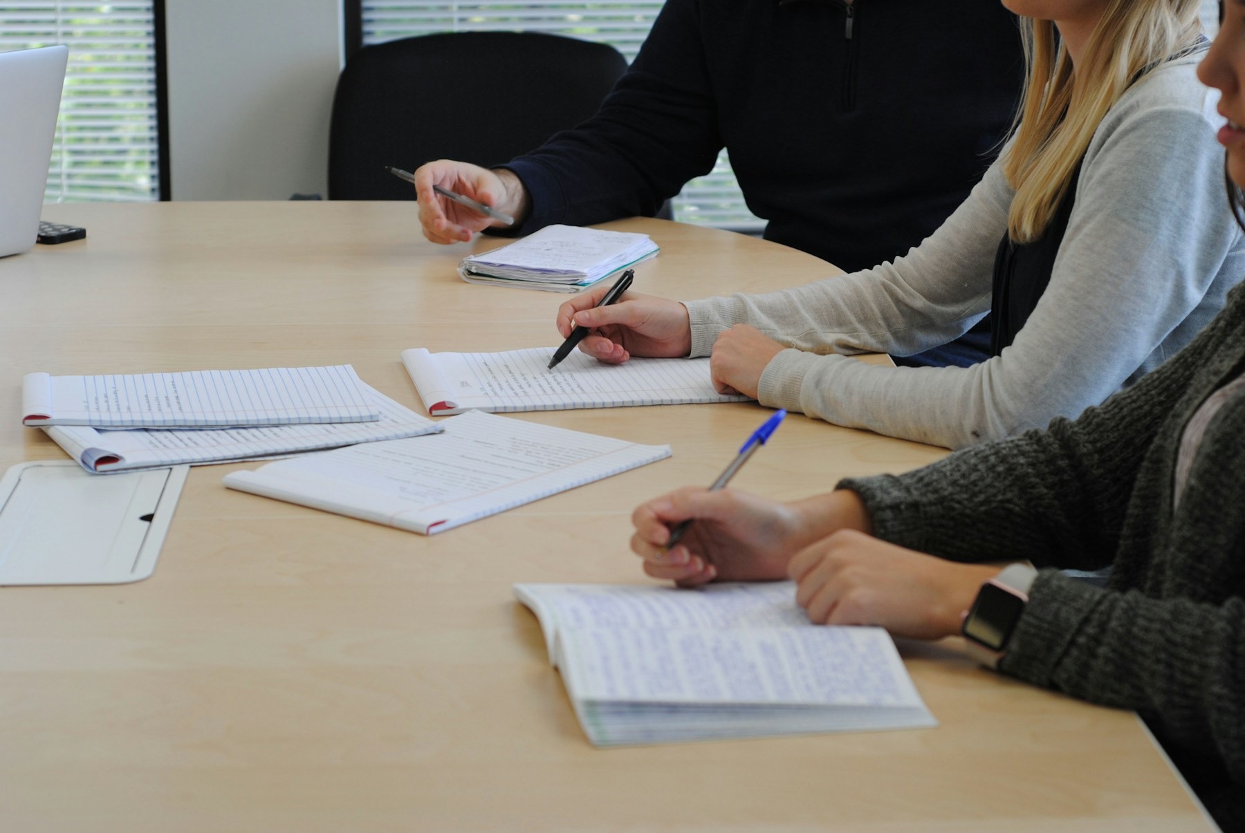 Trois personnes prenant des notes autour d'une table de réunion, visages hors champ.