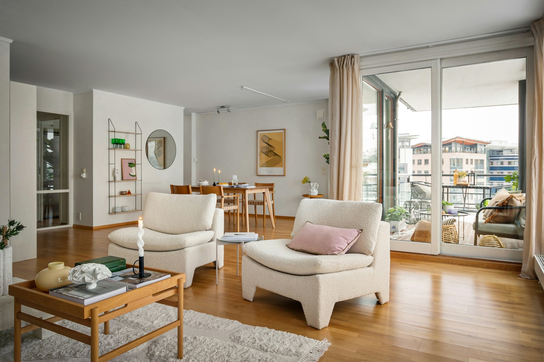 Salon lumineux d'appartement avec parquet, fauteuils clairs et baie vitrée donnant sur un balcon.